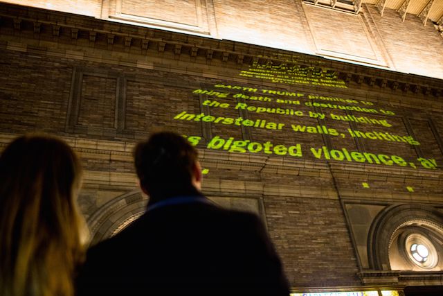 Onlookers read messages projected by members of The Illuminator, encouraging voters to oppose Donald Trump